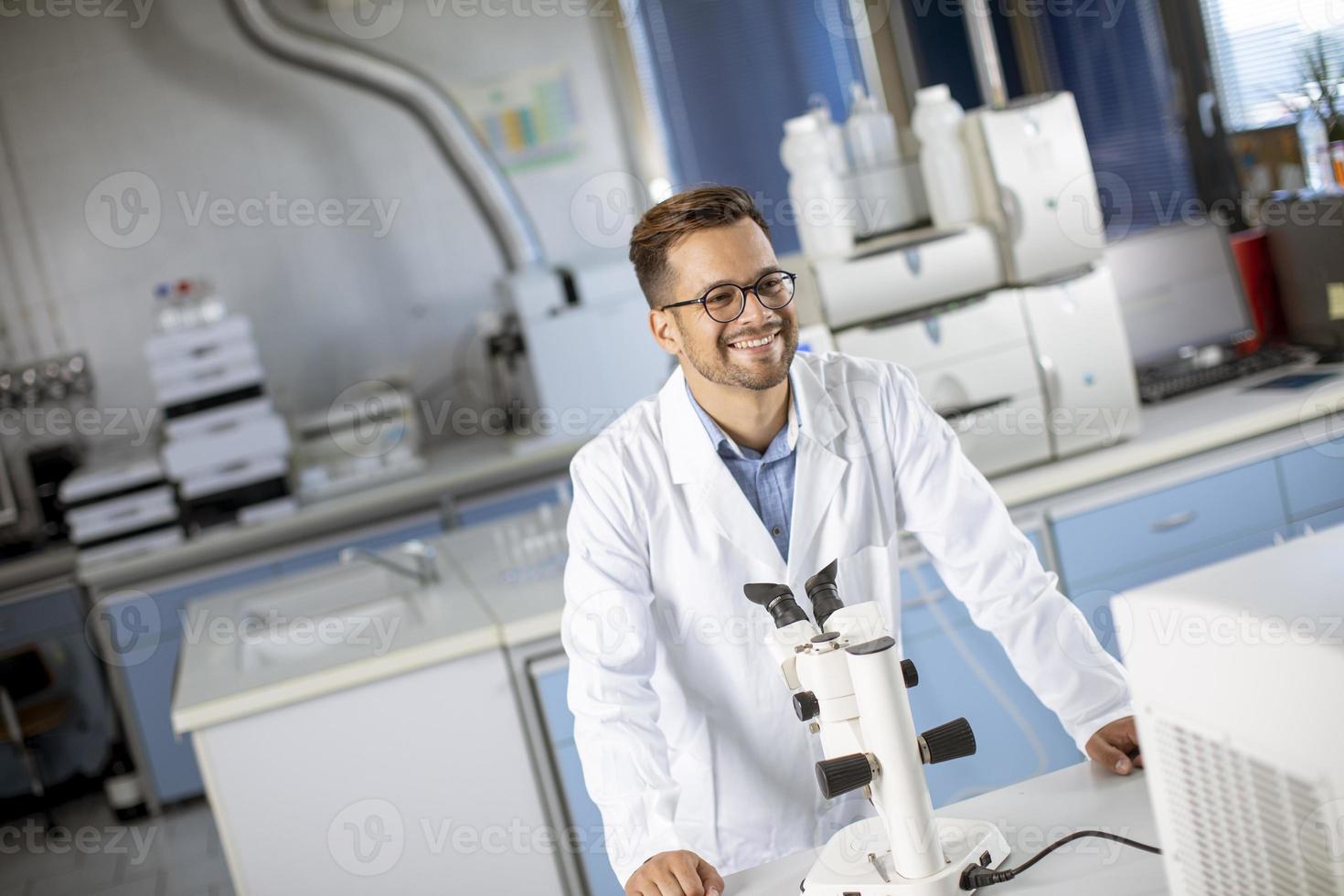 jovem cientista vestindo jaleco branco trabalhando com microscópio binocular no laboratório de ciências materiais foto