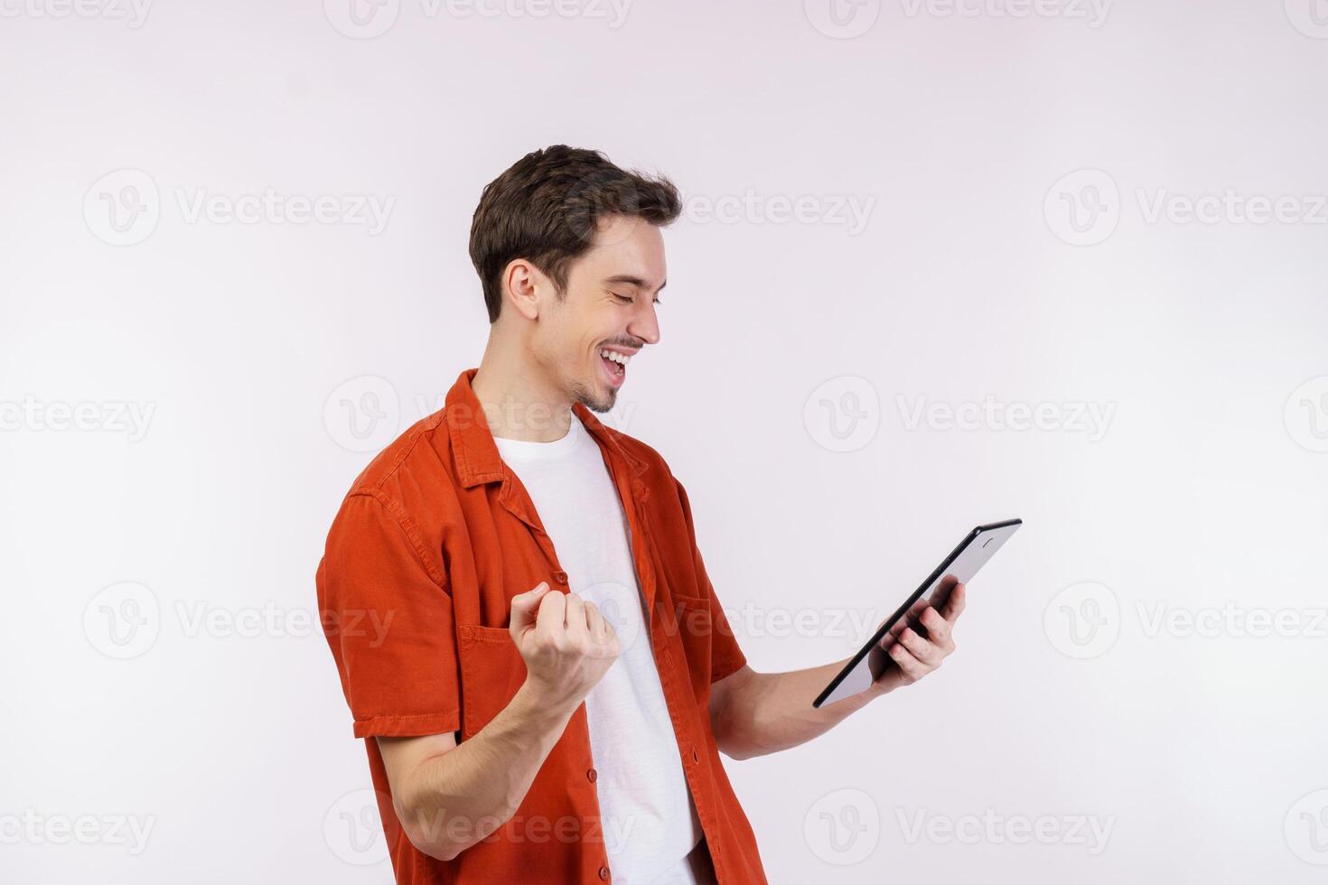 retrato do atraente alegre homem fazendo vencedora gesto aperto punho e usando dispositivo aplicativo procurando rede isolado sobre branco cor fundo foto