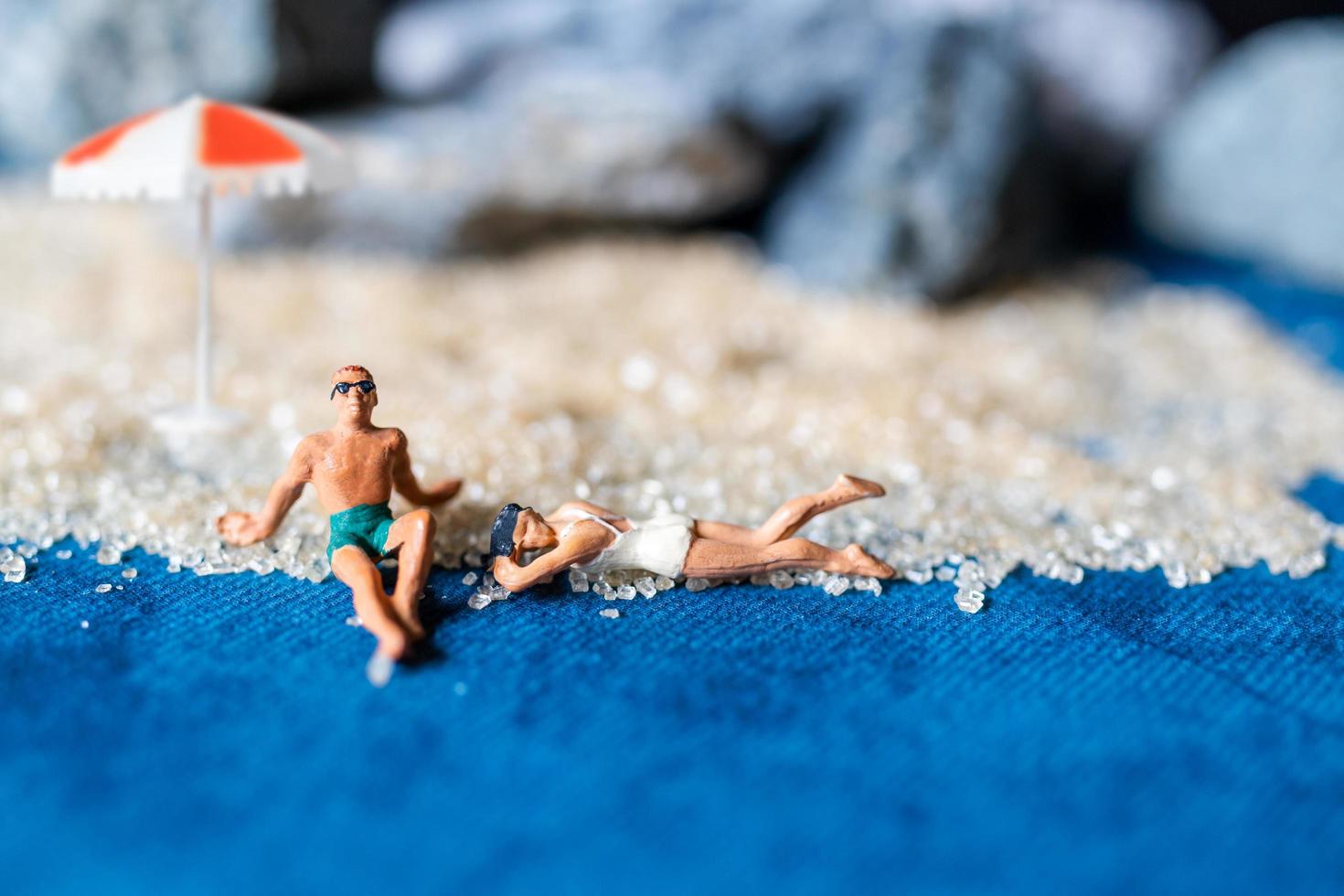 pessoas em miniatura usando maiôs relaxantes na praia com um fundo azul, conceito de verão foto