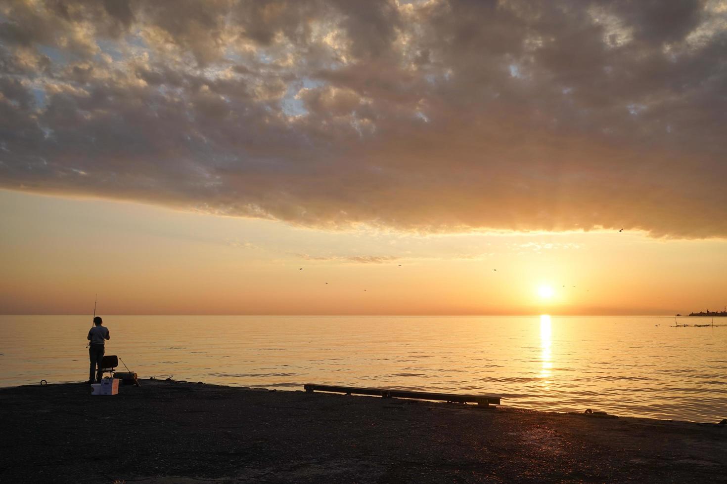 silhueta de um homem pescando em um píer com um pôr do sol colorido e nublado foto