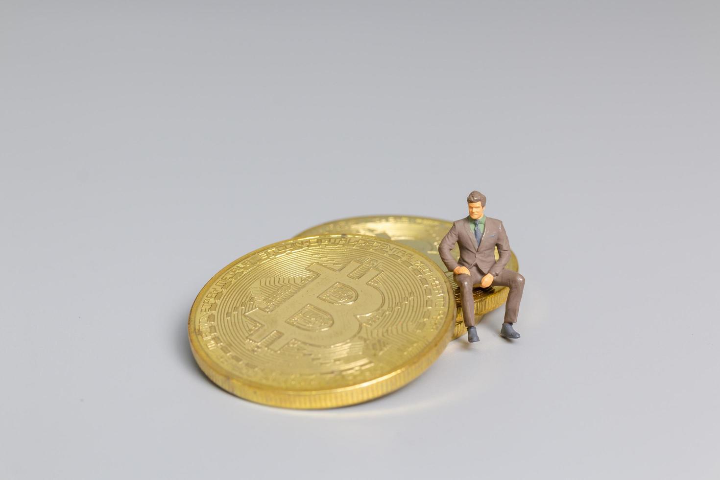 empresário em miniatura sentado sobre moedas bitcoin, conceito de investimento futuro foto