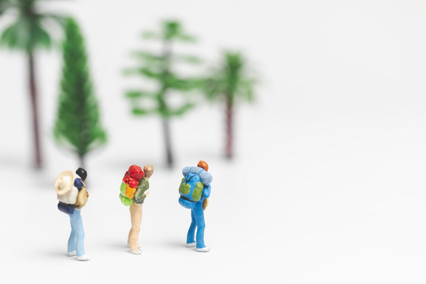 viajantes em miniatura com mochilas caminhando sobre um fundo branco, conceito de viagem e aventura foto