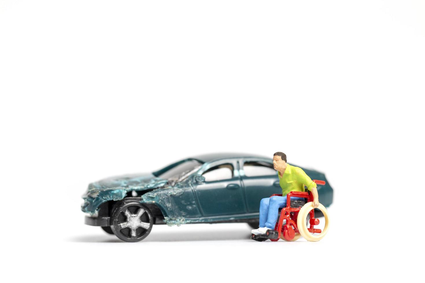 homem em miniatura em uma cadeira de rodas em um acidente de carro em um fundo branco foto
