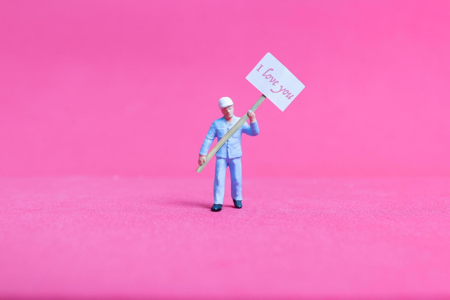 pessoa em miniatura segurando uma placa de papel com eu te amo em um fundo rosa, conceito de dia dos namorados foto