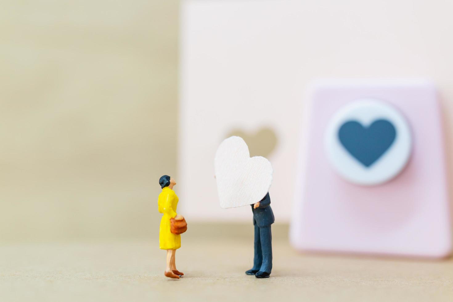 casal em miniatura com um coração de papel sobre fundo de madeira, conceito de dia dos namorados foto