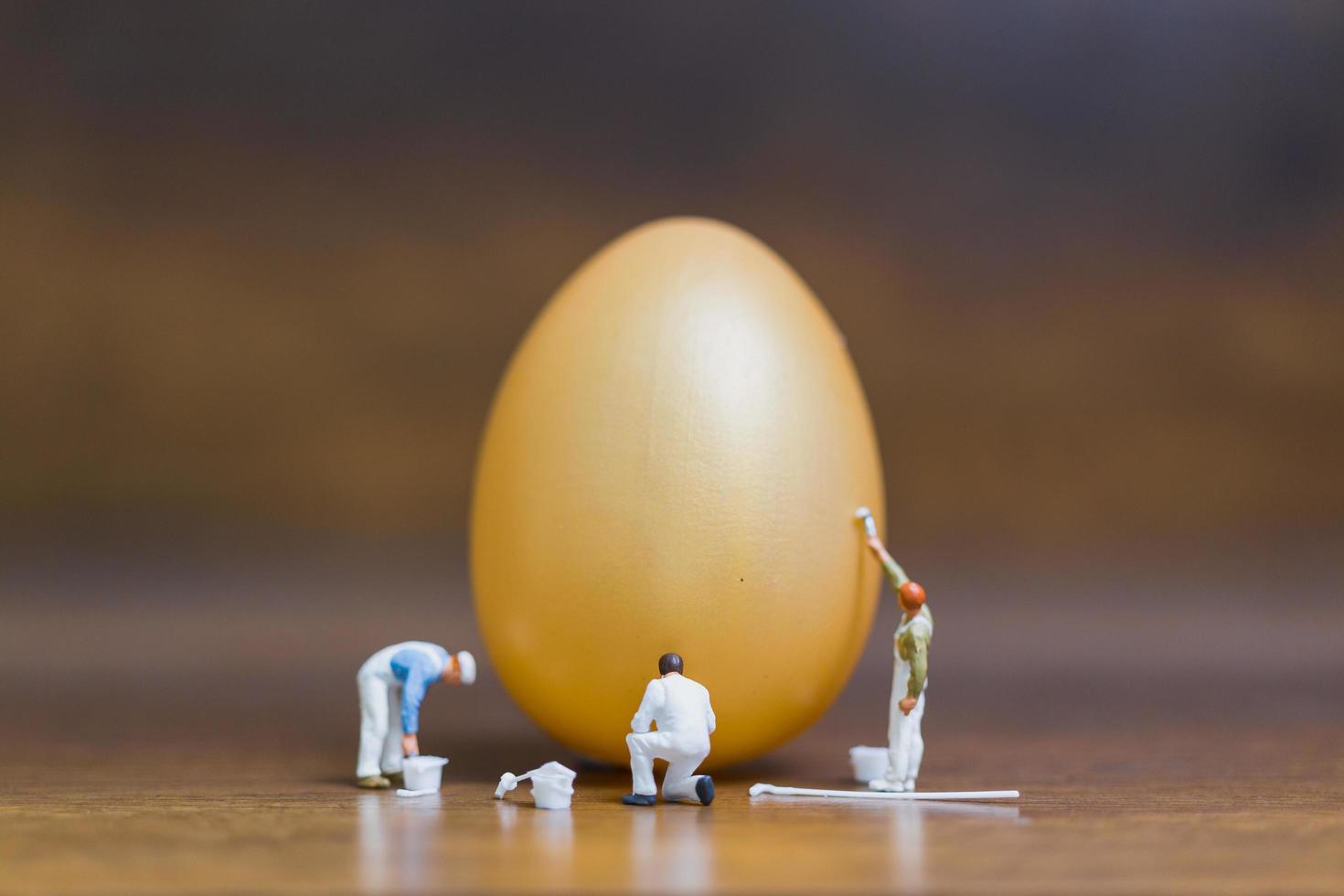 pintores em miniatura pintando ovos de páscoa em um fundo de madeira foto