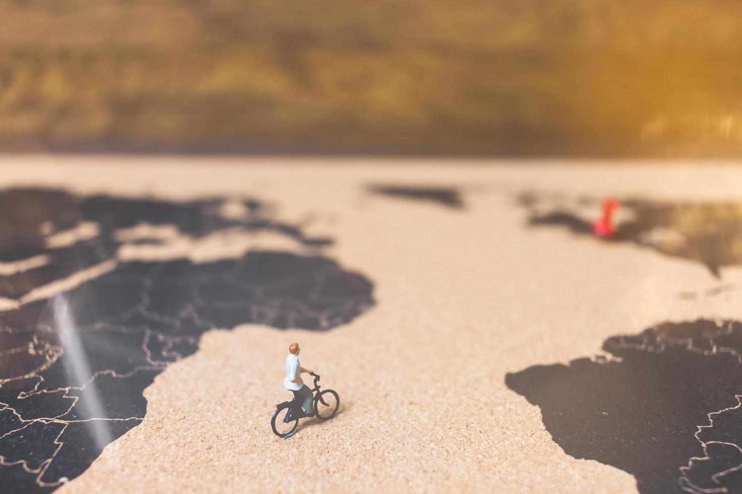 viajantes em miniatura andando de bicicleta em um mapa-múndi, viajando e explorando o conceito do mundo foto