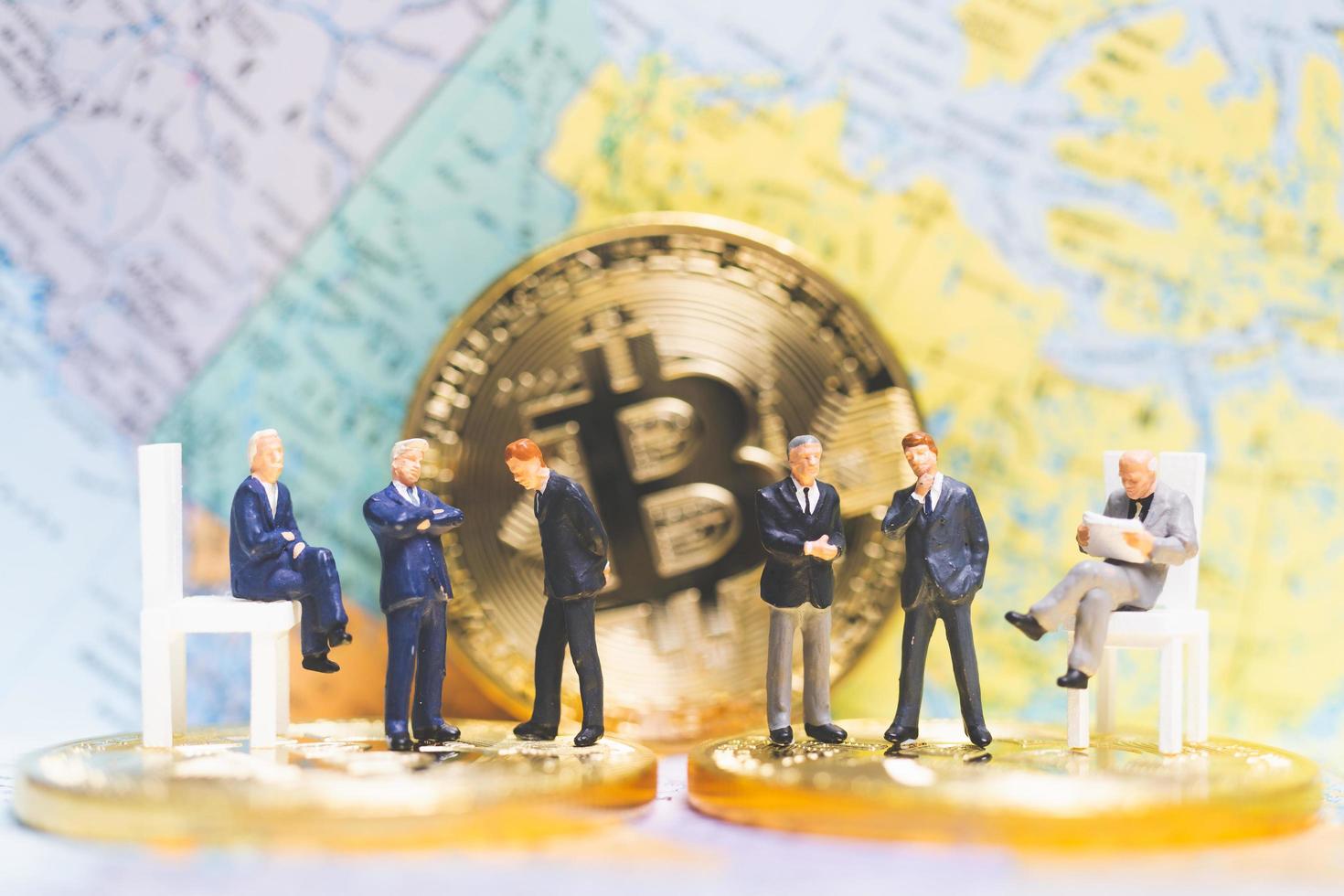 empresários em miniatura em uma pilha de moedas de criptomoeda com um mapa-múndi ao fundo, dinheiro e conceito de sucesso de negócios financeiros foto