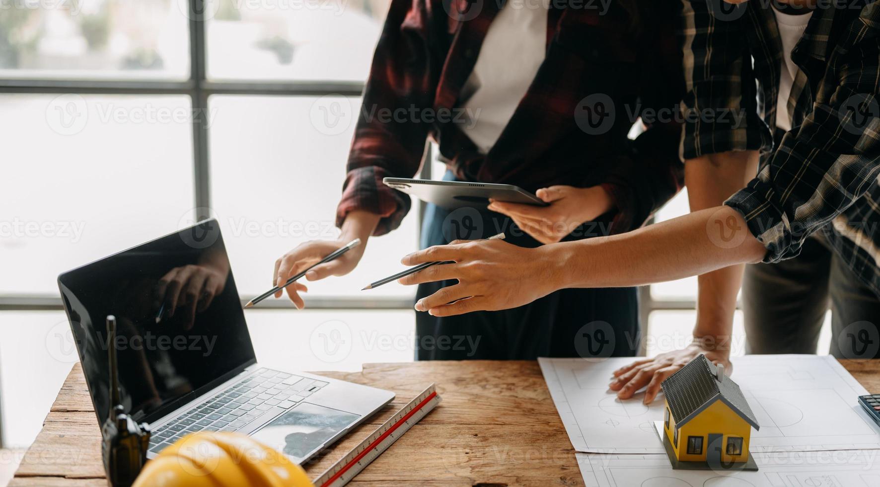 dois colegas discutindo dados de trabalho e tablet, laptop com projeto arquitetônico no canteiro de obras na mesa no escritório foto