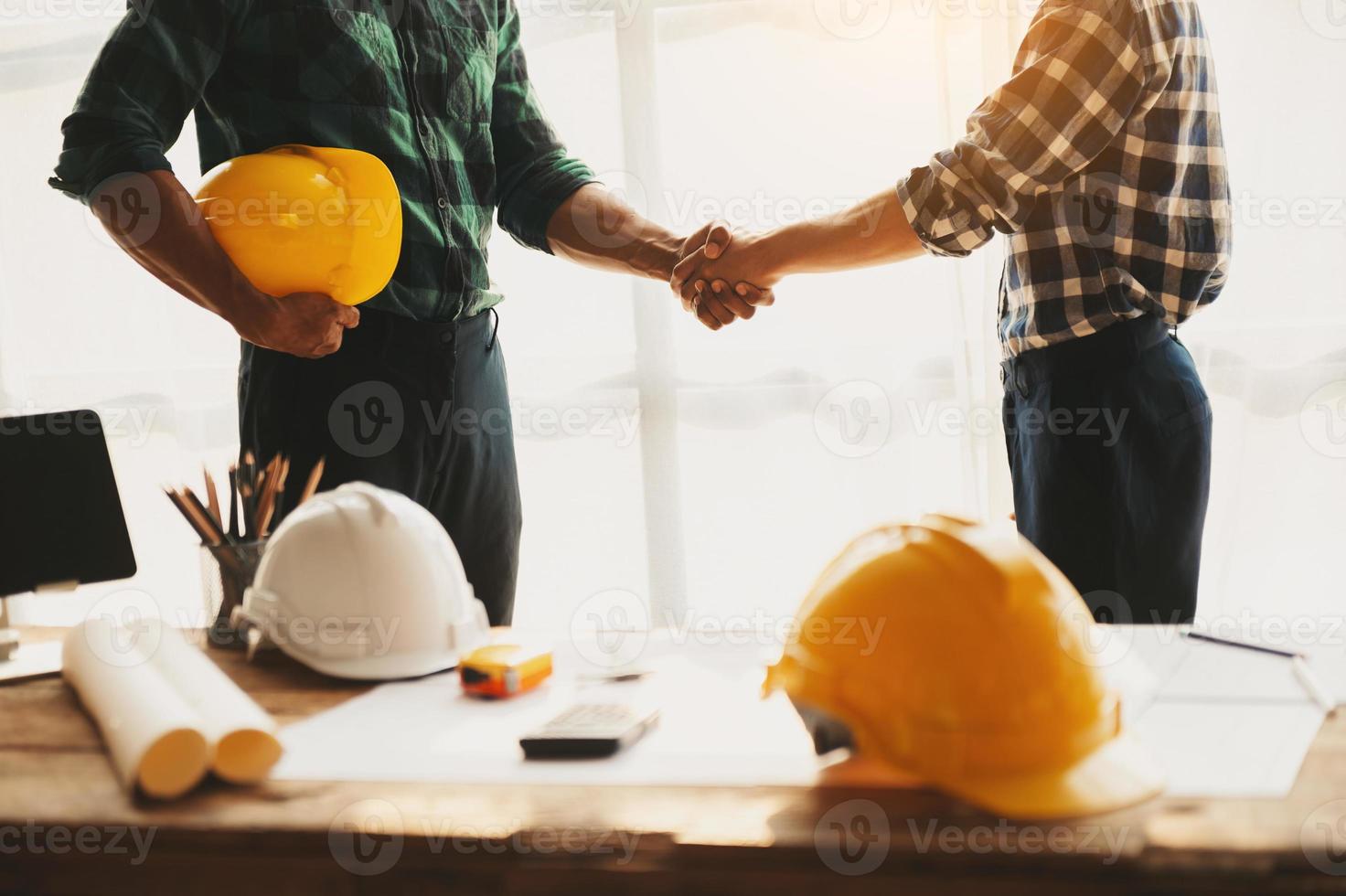 construção equipe mexe mãos cumprimento começar Novo projeto plano atrás amarelo capacete em escrivaninha dentro escritório para consulta sobre seus construção projeto.. foto