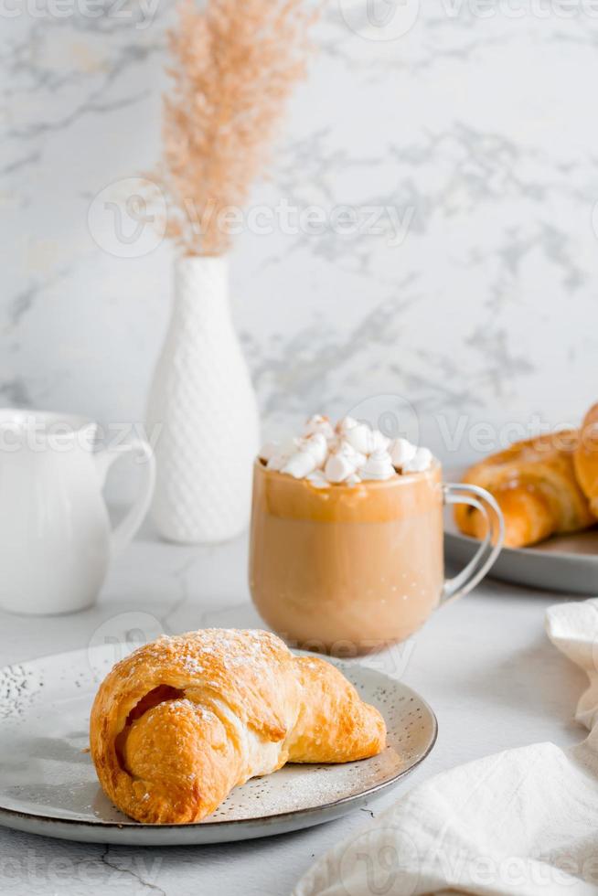 delicioso café com marshmallows e croissants em pratos em a mesa. estilo de vida caseiro lanche. vertical Visão foto