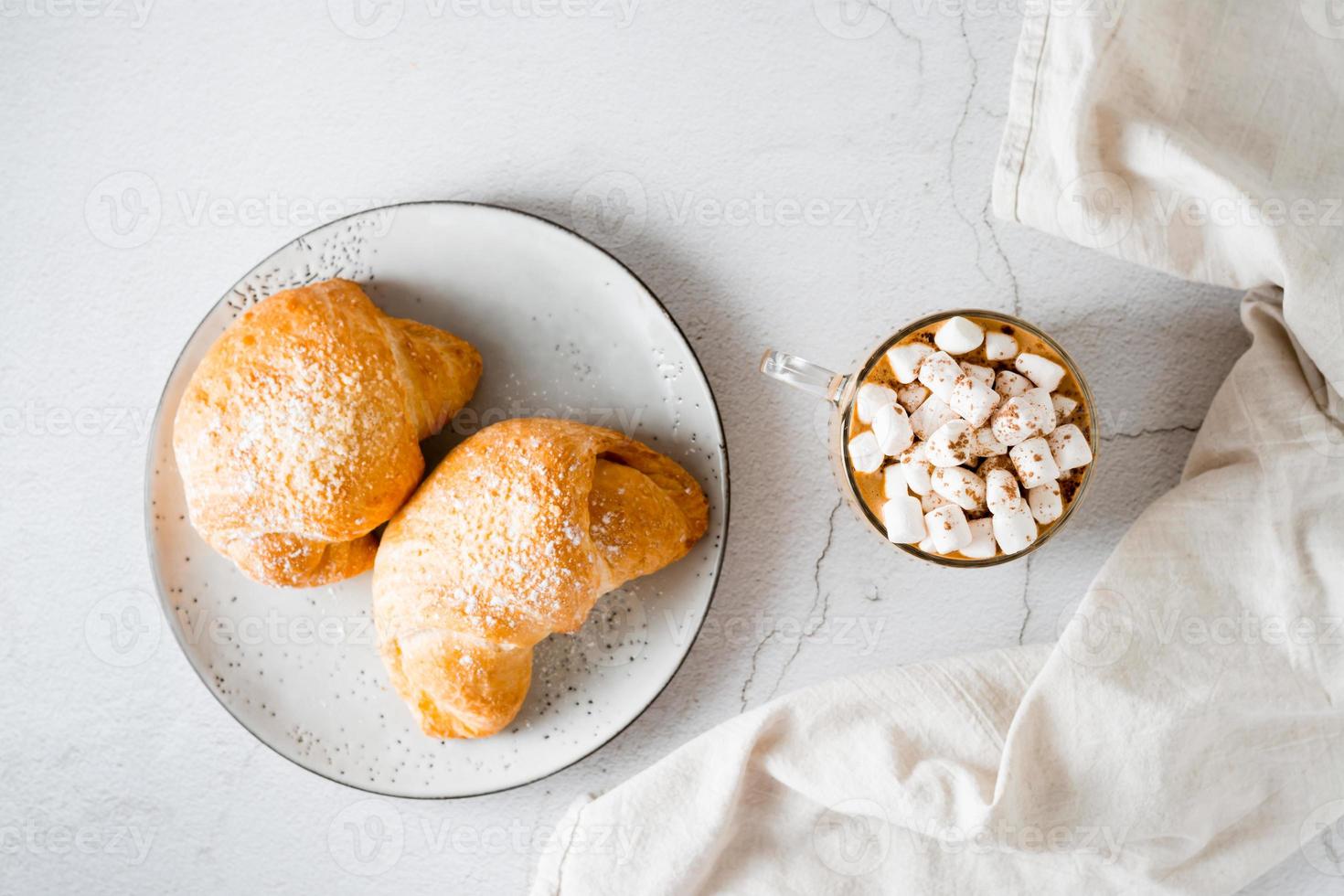 copo do café com marshmallows e croissants em uma prato em a mesa. caseiro café da manhã estilo de vida. topo Visão foto