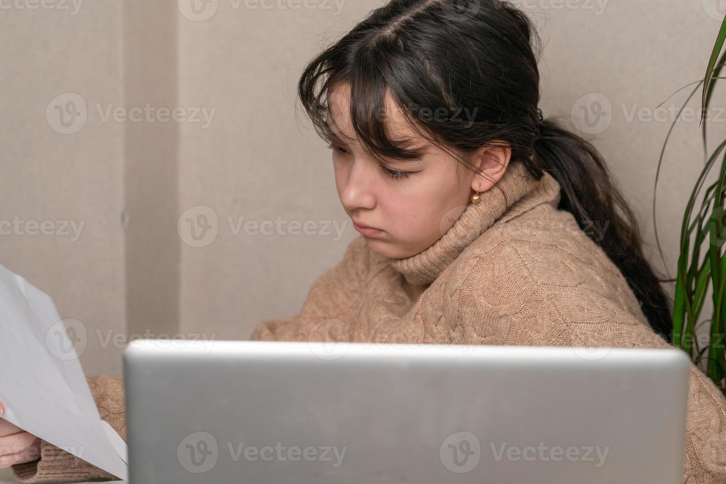 garota trabalha com documentos sentado na frente de um laptop em sua mesa foto