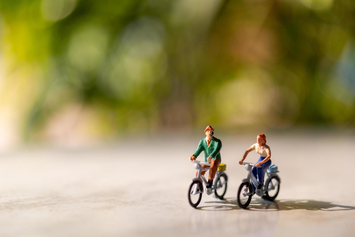 pessoas em miniatura andando de bicicleta ao ar livre com um fundo verde bokeh, conceito de esporte e viagem foto