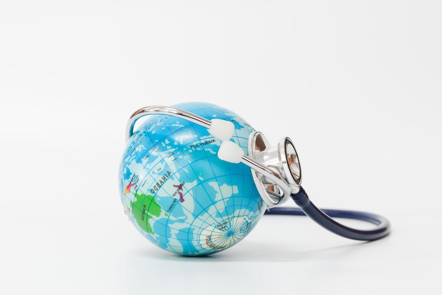 estetoscópio enrolado ao redor de um globo em um fundo branco., conceito de salvar o mundo foto