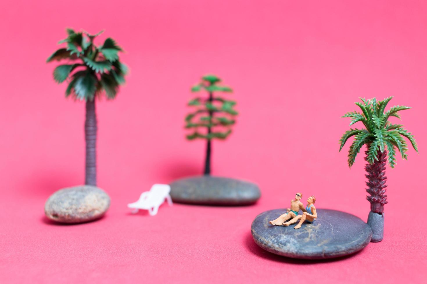 pessoas em miniatura usando maiôs relaxando em uma rocha com um fundo rosa foto