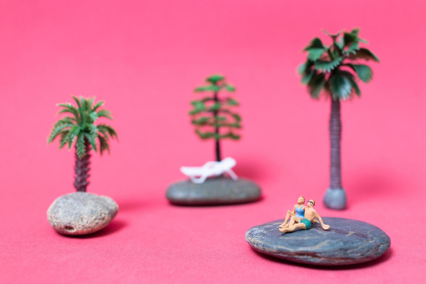 pessoas em miniatura usando maiôs relaxando em uma rocha com um fundo rosa foto