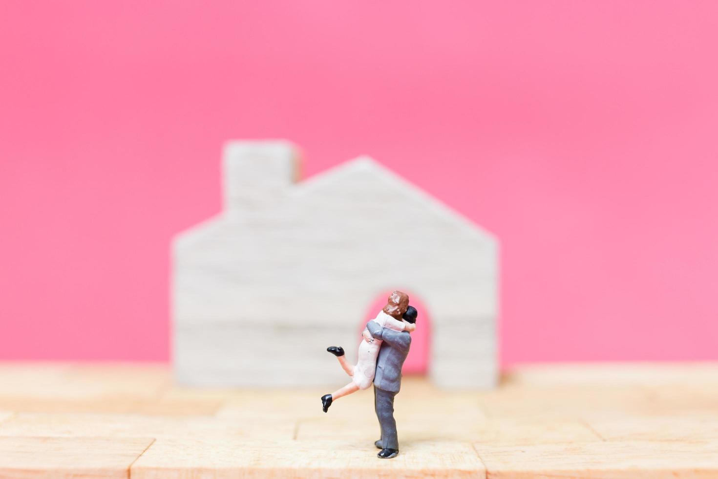casal em miniatura com casas em um fundo rosa, conceito de dia dos namorados foto