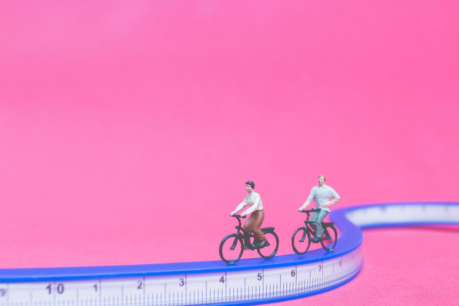 viajantes em miniatura com bicicletas em uma ponte azul em um fundo rosa foto