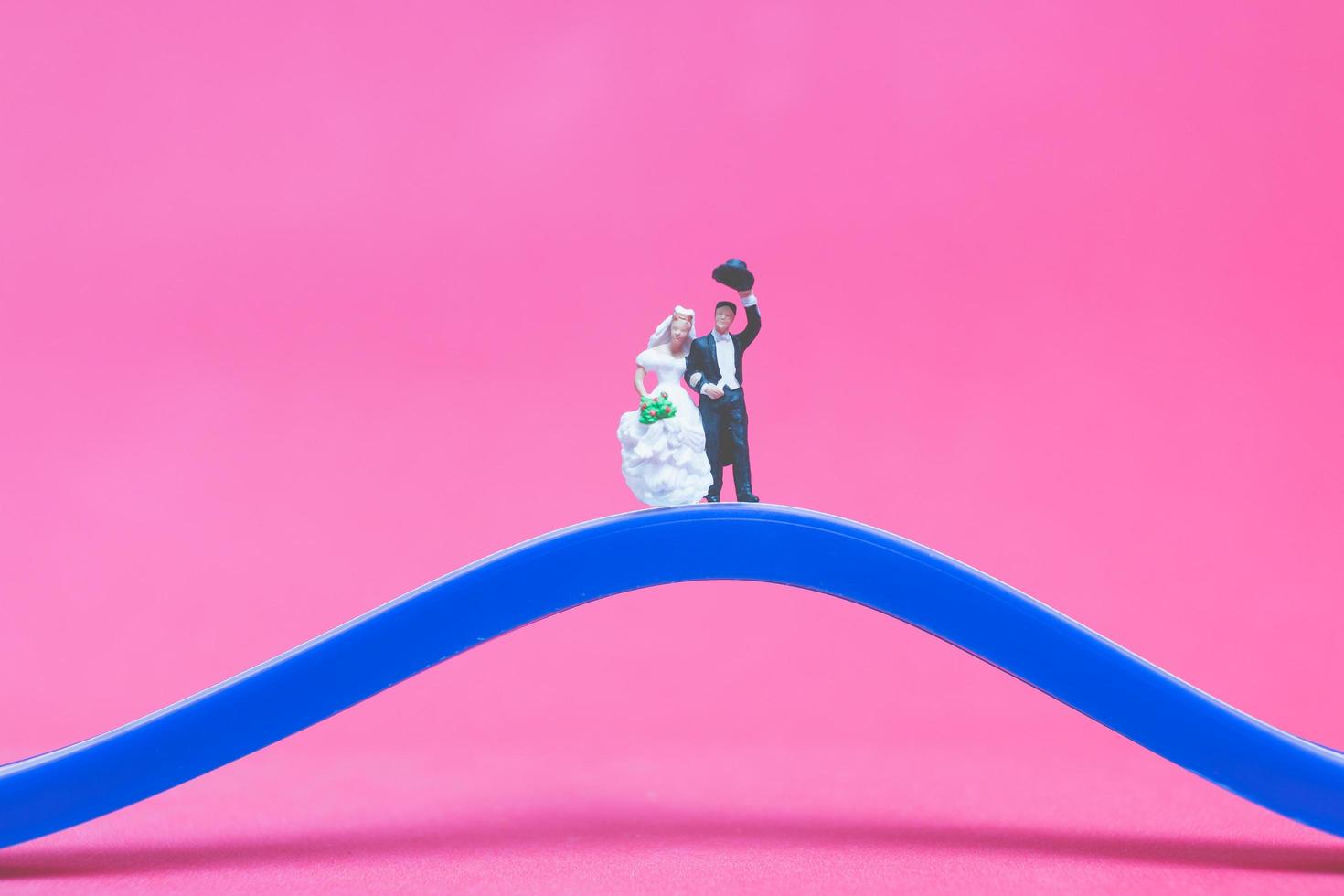 casamento em miniatura, uma noiva e um noivo em uma ponte sobre um fundo rosa foto