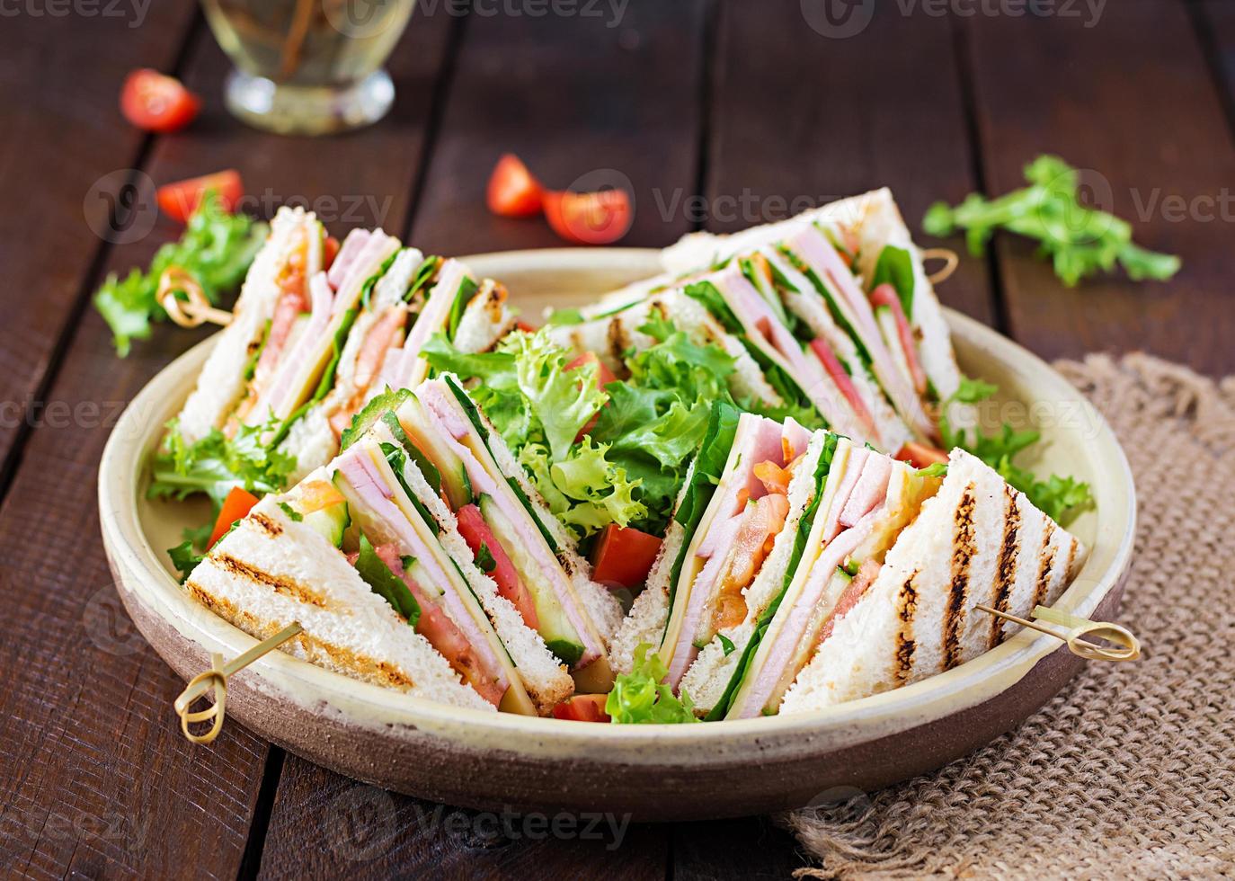 clube sanduíche com presunto, tomate, pepino, queijo, e Rúcula em de madeira fundo. foto