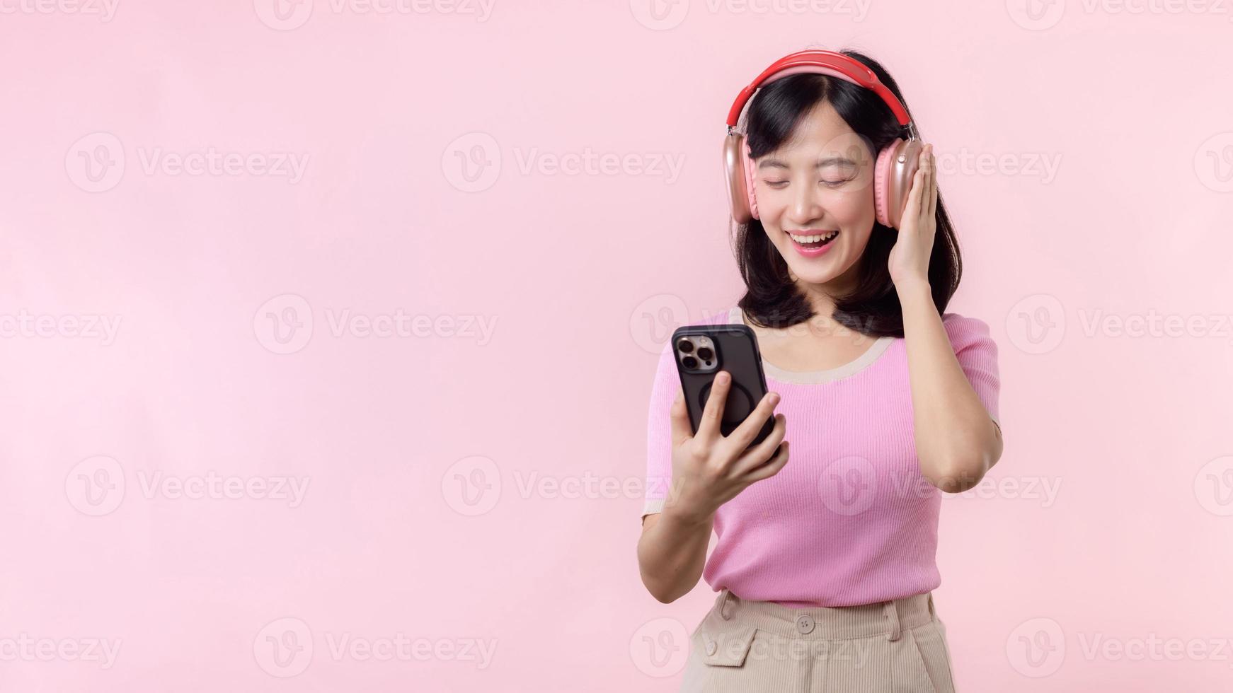 retrato alegre jovem ásia mulher apreciar ouvindo audio de Smartphone música inscrição contra Rosa. feliz sorridente fêmea pessoa com fone de ouvido. som, lazer, estilo de vida, tecnologia conceito foto