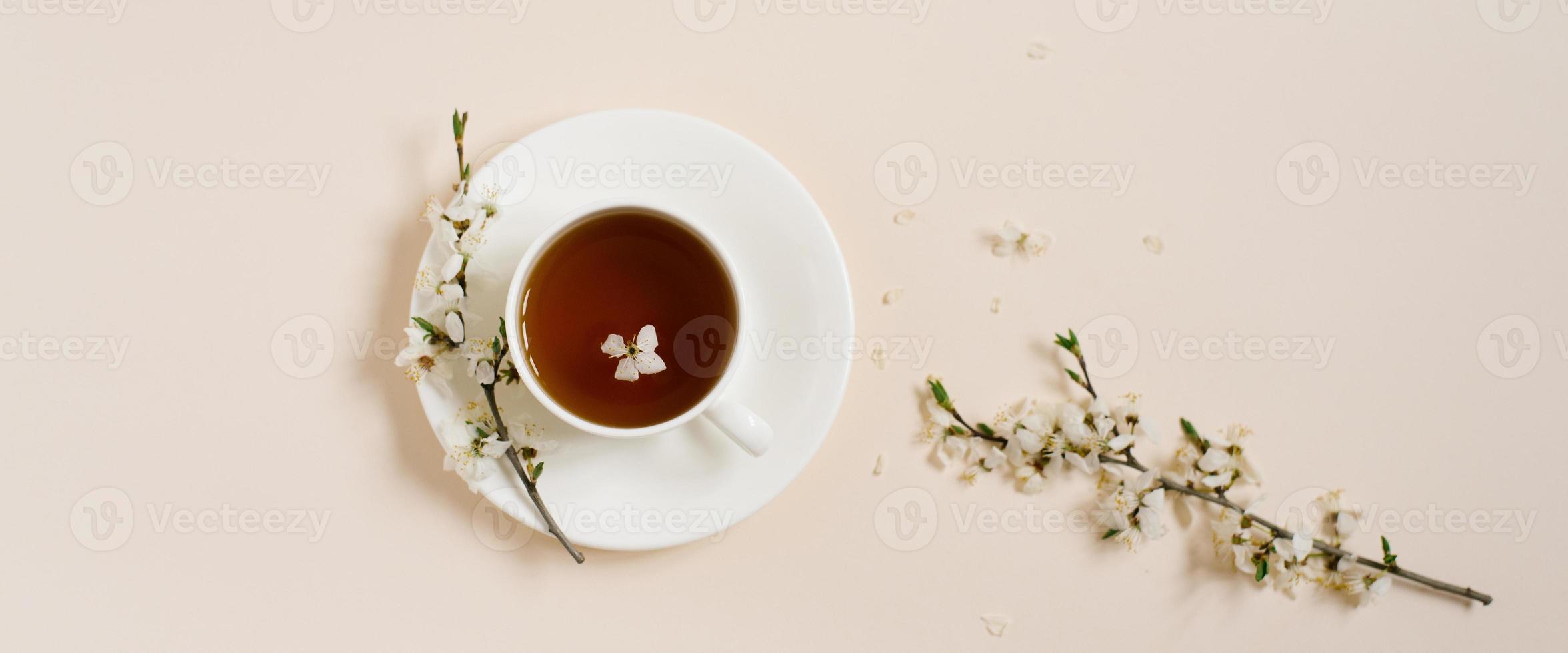 branco porcelana copo com Preto chá e marshmallows. galhos do uma florescendo maçã árvore mentira em uma bege fundo. Primavera conceito. baner foto