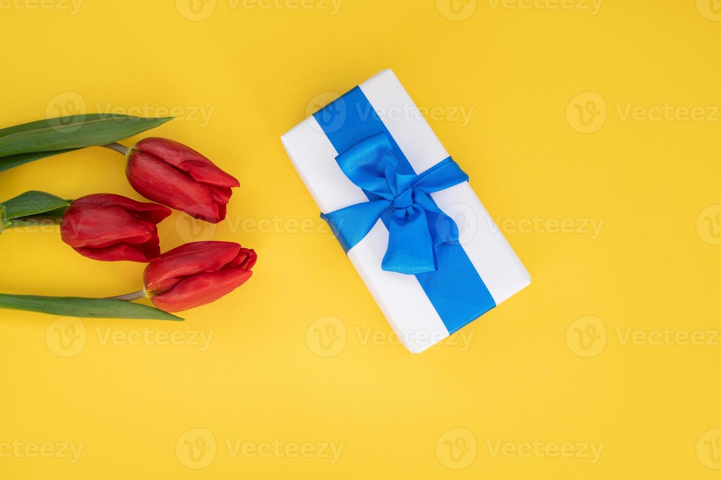 topo Visão do amarelo mesa com presente caixa com azul fita e tulipas. foto