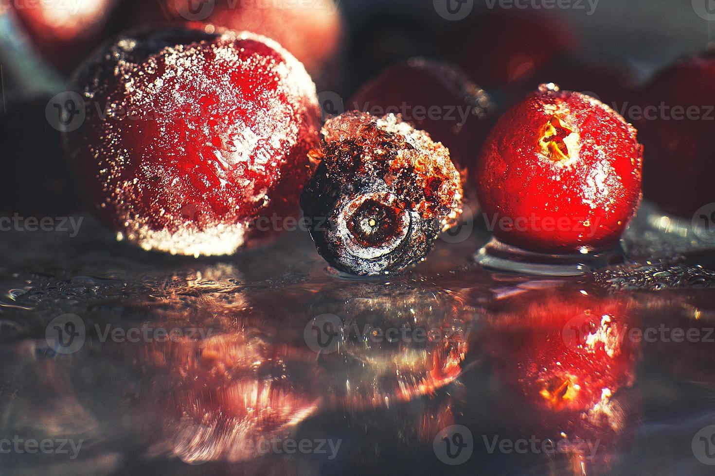 fechar-se congeladas bagas em a vidro com reflexão . congeladas bagas em uma Sombrio fundo macro. cranberries amoras e cerejas foto