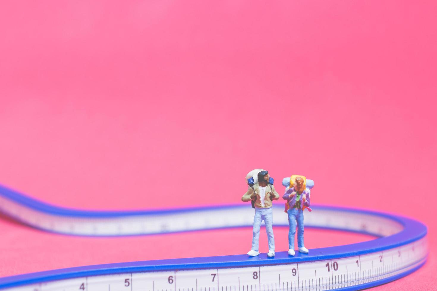 casal de viajantes em miniatura em uma ponte com um fundo rosa foto