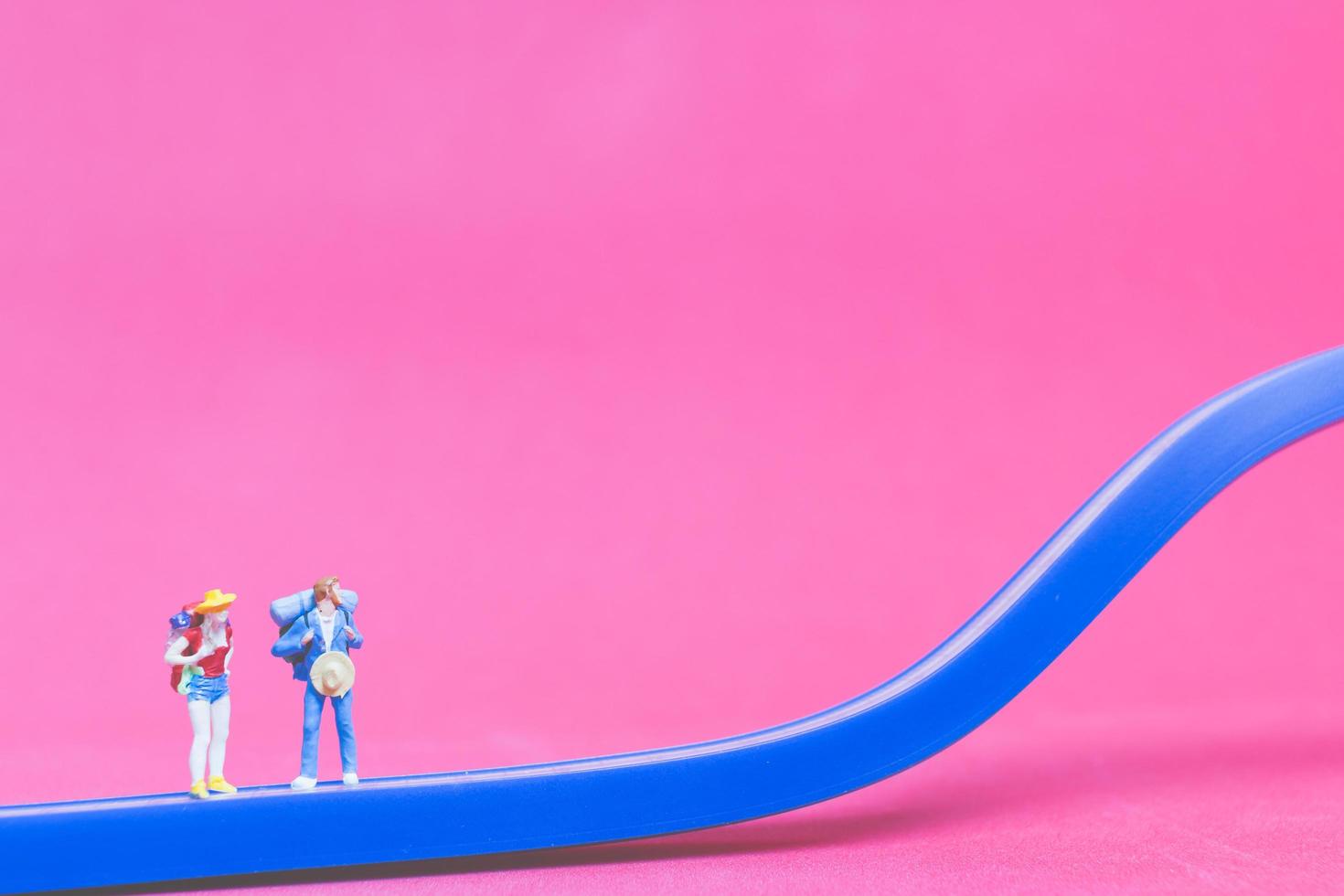 casal de viajantes em miniatura em uma ponte com um fundo rosa foto