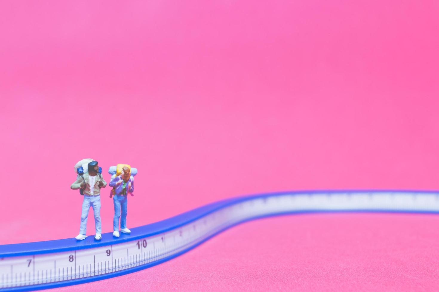 casal de viajantes em miniatura em uma ponte com um fundo rosa foto