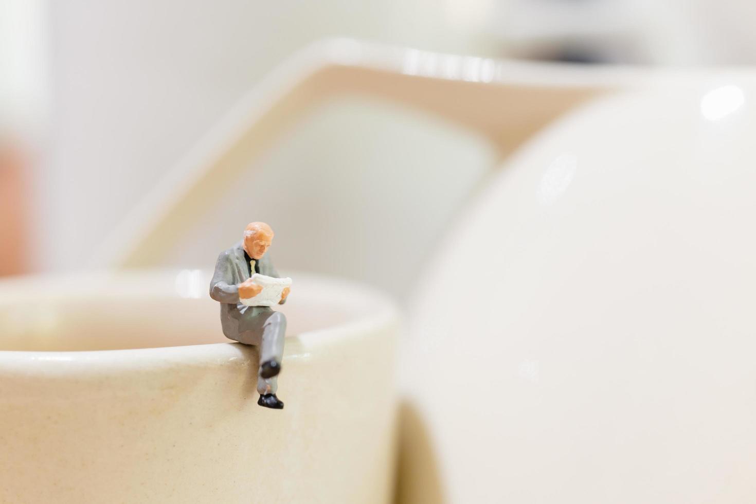 empresário em miniatura sentado em uma xícara de chá foto