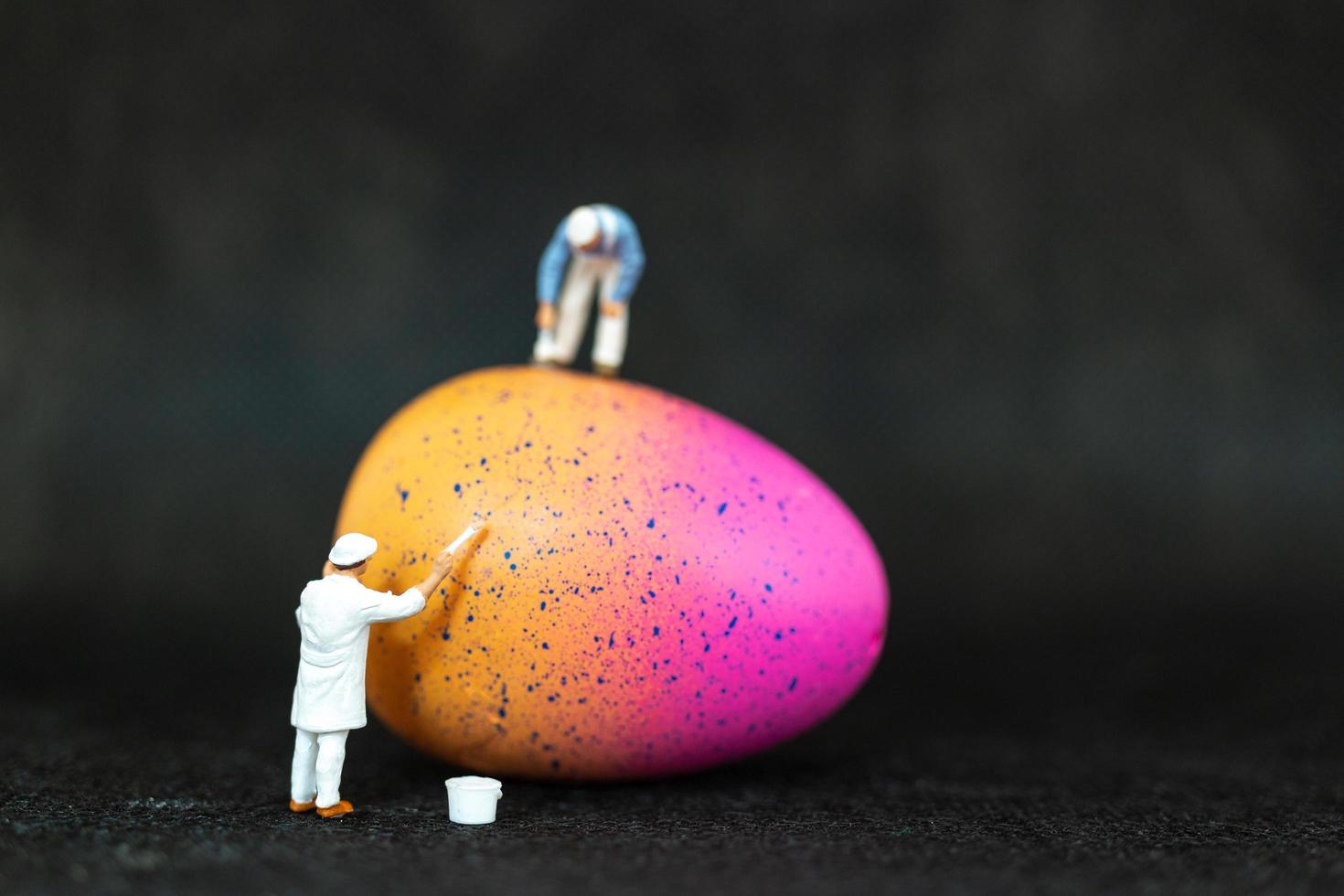 pessoas em miniatura pintando ovos de páscoa para o dia de páscoa em um fundo preto foto