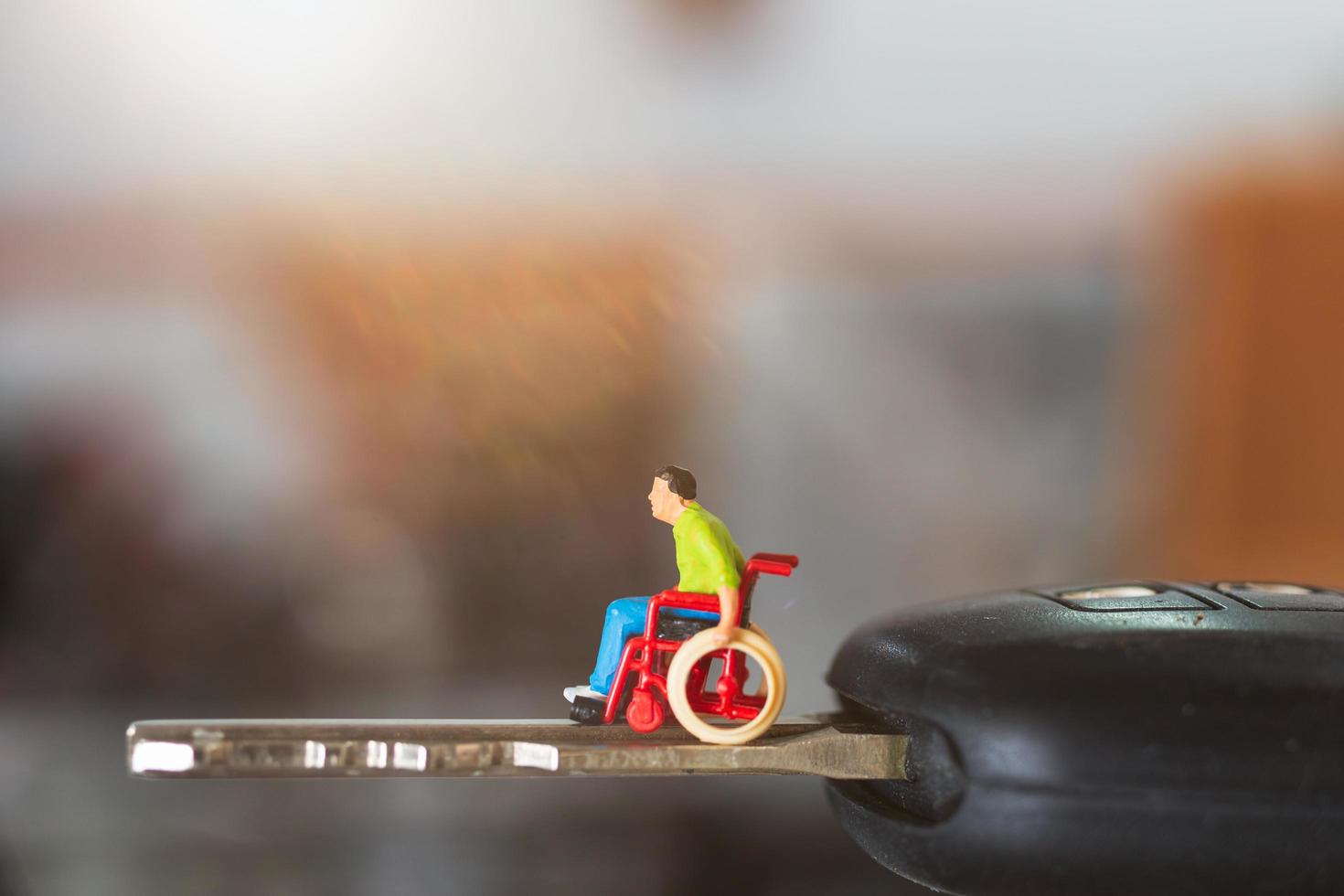 homem deficiente em miniatura sentado em uma cadeira de rodas na chave de um carro foto
