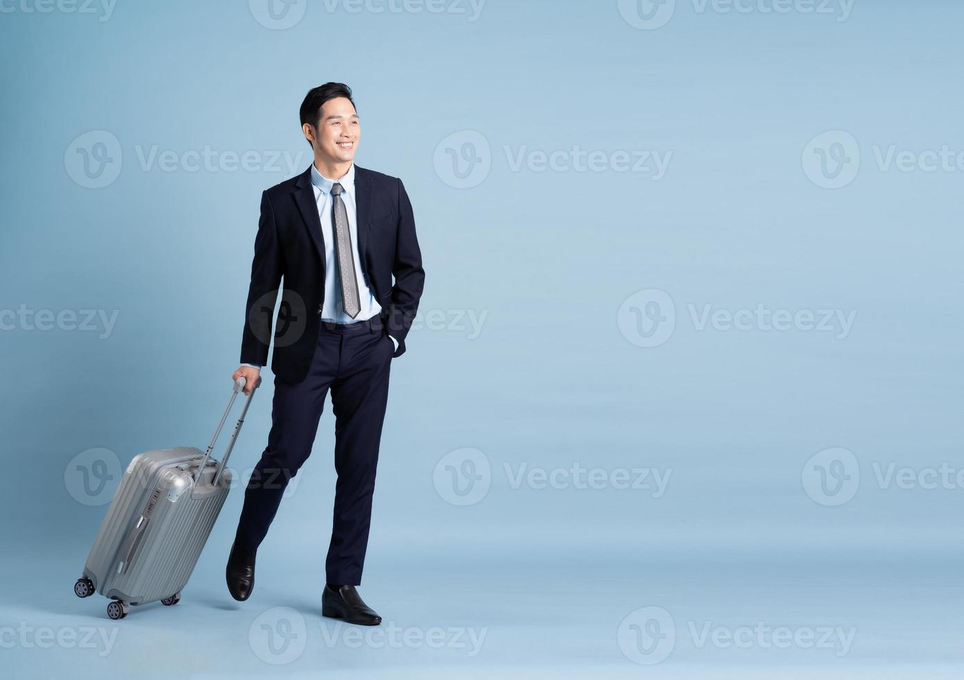 retrato do ásia homem de negocios vestindo uma terno e puxar uma mala de viagem foto