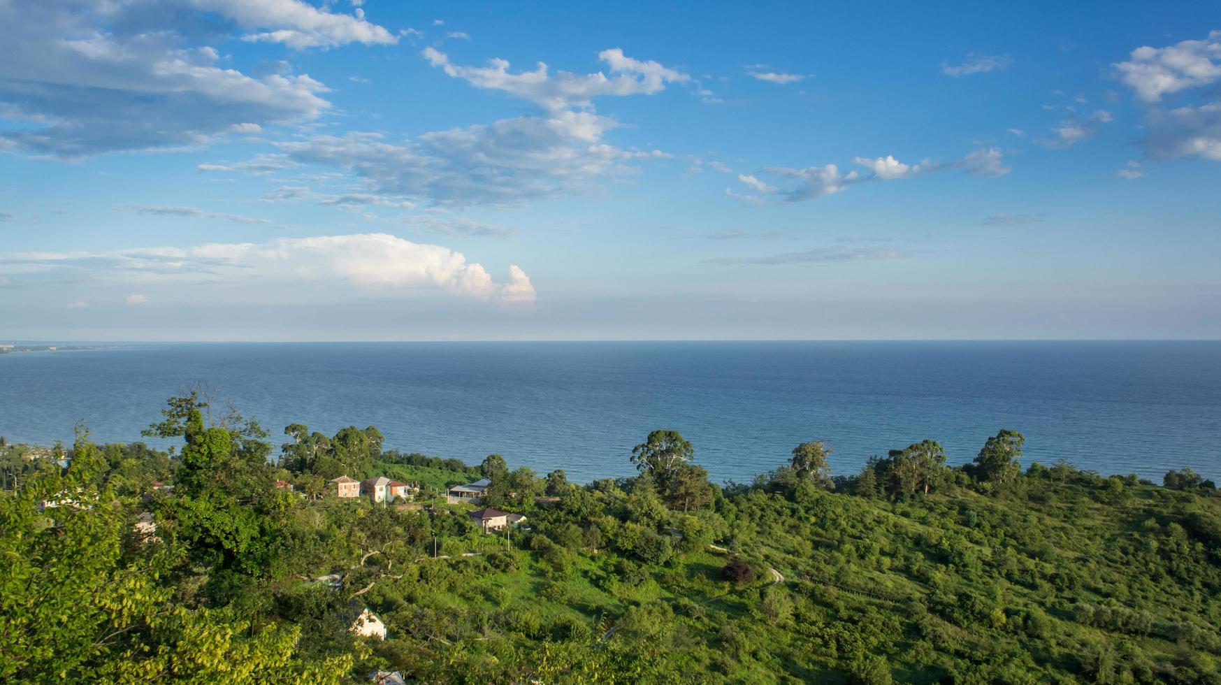 paisagem marinha com casas e campos verdes ao lado de um corpo de água com céu azul nublado em new athos, abkhazia, georgia foto