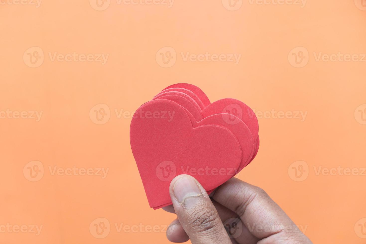 segurando corações vermelhos em fundo laranja foto