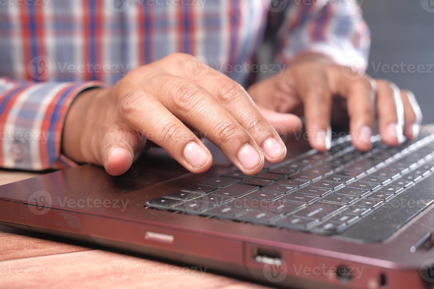 feche a mão do homem digitando no laptop foto