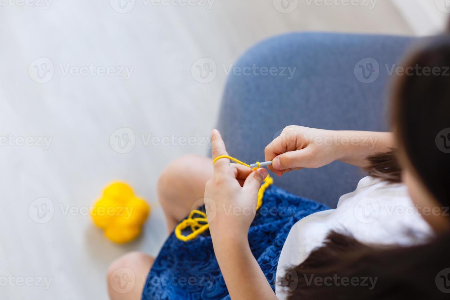 pequeno menina malhas crochê. a menina senta em a sofá e malhas a partir de tricô fio. crochê Grosso tópicos. casa conforto. foto