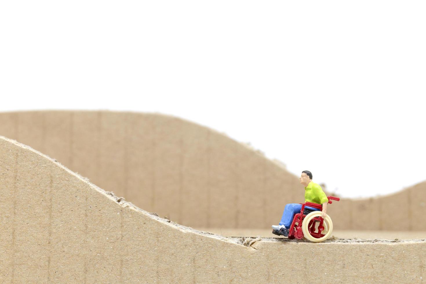 homem em miniatura em uma cadeira de rodas em um recorte de papelão isolado em um fundo branco foto