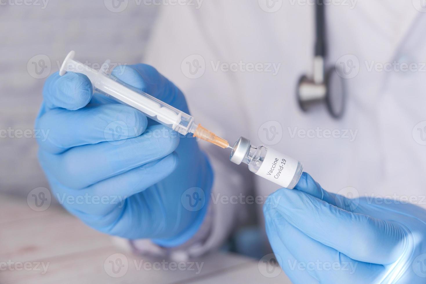 médico com luvas médicas segura seringa e vacina covid-19 foto