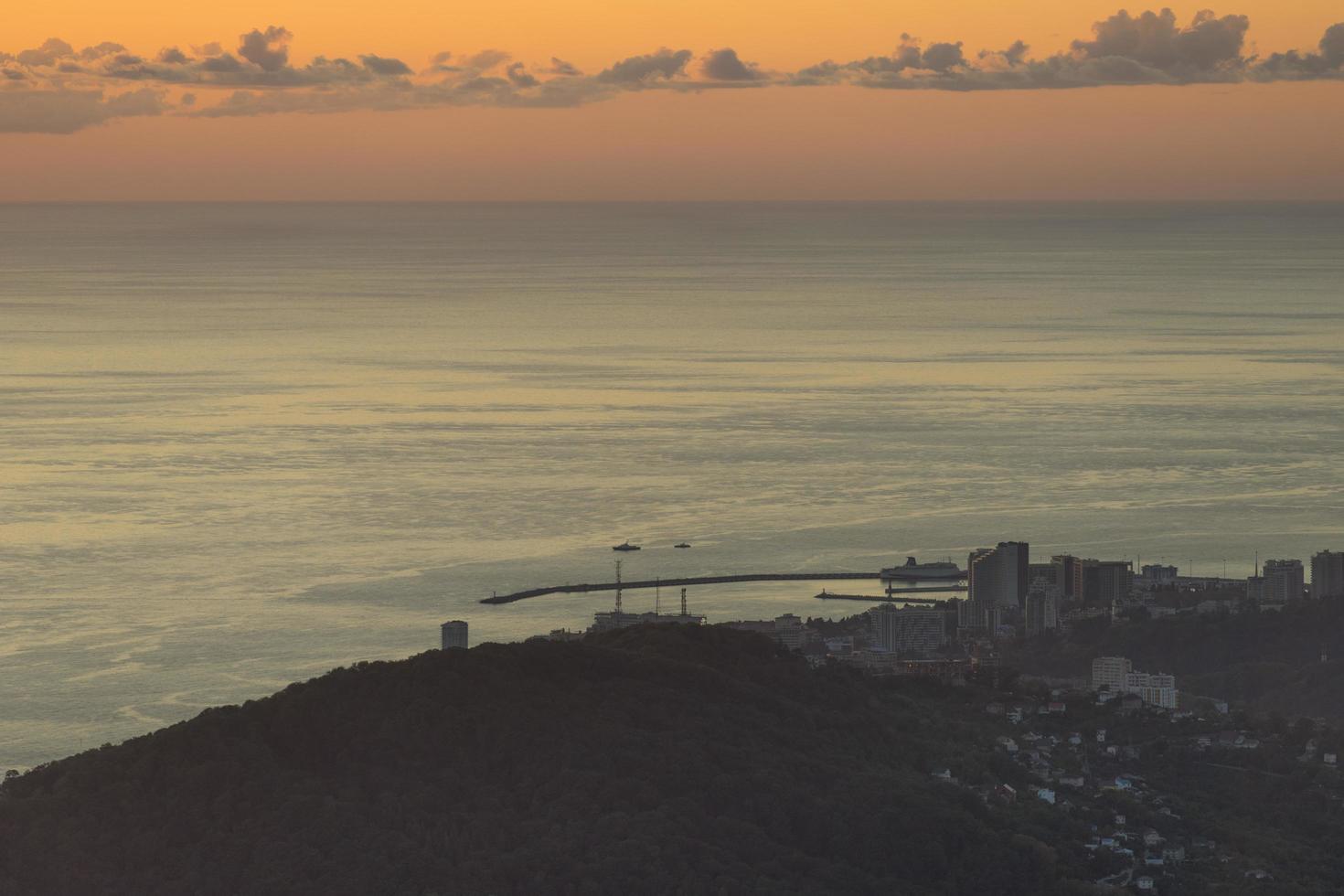 vista aérea de montanhas e cidade distante ao lado de corpo d'água com céu nublado colorido em sochi, rússia foto