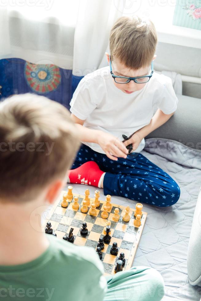 Rapazes jogando de madeira xadrez sentado em uma cinzento sofá dentro frente do a janela, topo Visão foto