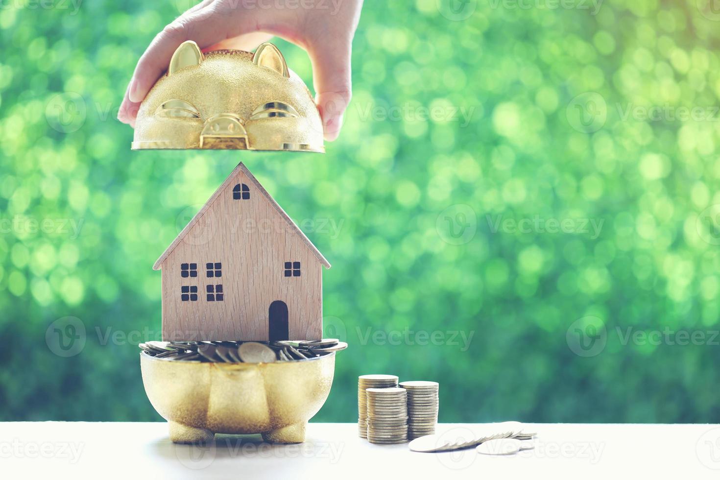 pilha de moedas em um cofrinho dourado com uma casa modelo em um fundo verde natural foto