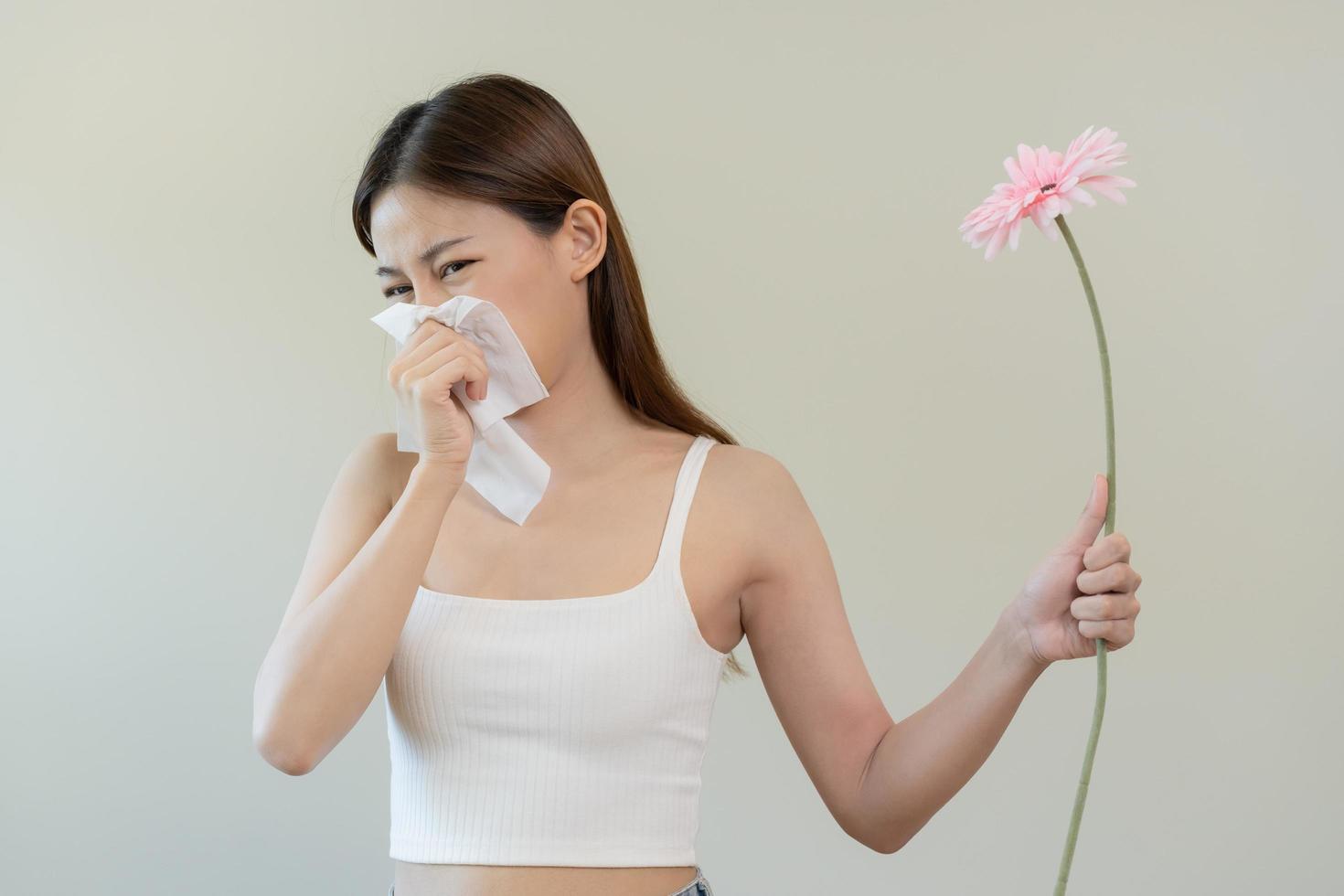 alérgico rinite sintoma do odor pólen floração, retrato ásia jovem mulher mão dentro espirrar, sopro escorrendo nariz depois de cheiro, malcheiroso a partir de flor flor, segurando longe Rosa flora em branco fundo. foto