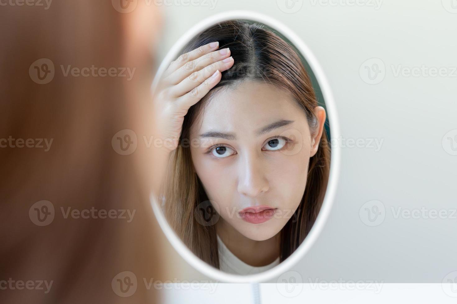 estragado cabelo, face sério ásia jovem mulher preocupação olhando às couro cabeludo dentro espelho, mão dentro pausa para dentro frente cabelo perda, fino problema sintoma às lar. saúde Cuidado xampu beleza, isolado em fundo. foto