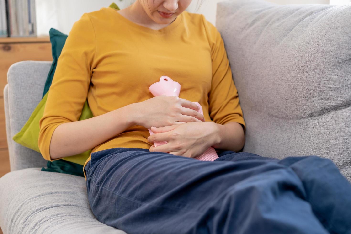 menstruação, período ciclo do por mês, doeu ásia jovem mulher, fêmea mão dentro dor de estômago, Sofra a partir de pré-menstrual, barriga ou abdômen dor, usando quente água garrafa. saúde problema inflamação dentro corpo. foto