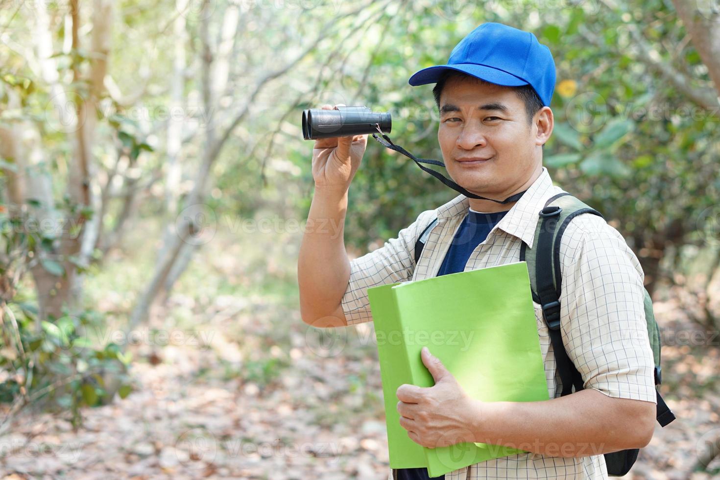 ásia homem explorador desgasta azul boné, detém binocular dentro floresta para pesquisa botânico plantas e criaturas animais selvagens. conceito, natureza exploração. ecologia e ambiente. foto