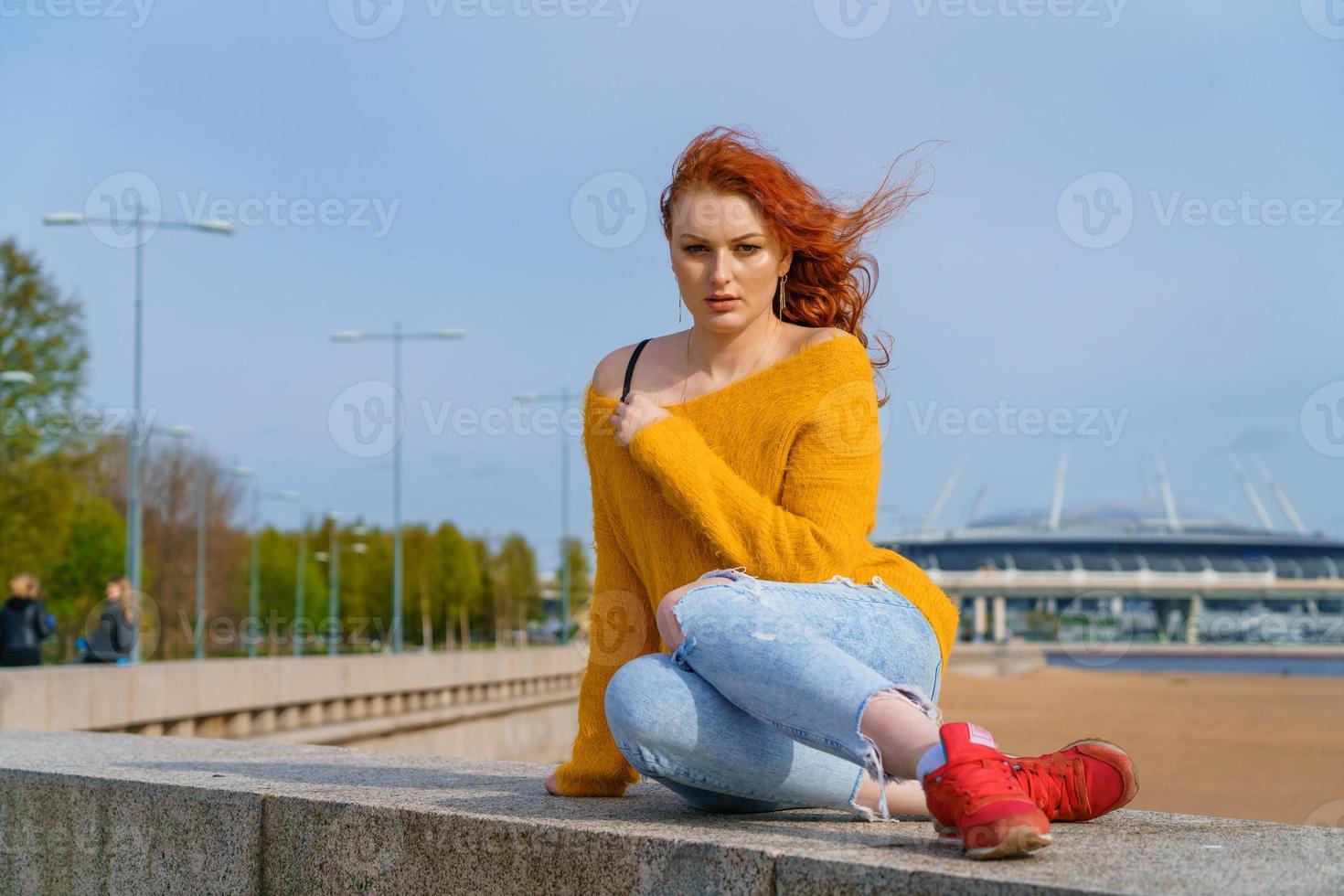 jovem ruivo menina dentro amarelo suéter e jeans. bonita mulher senta foto